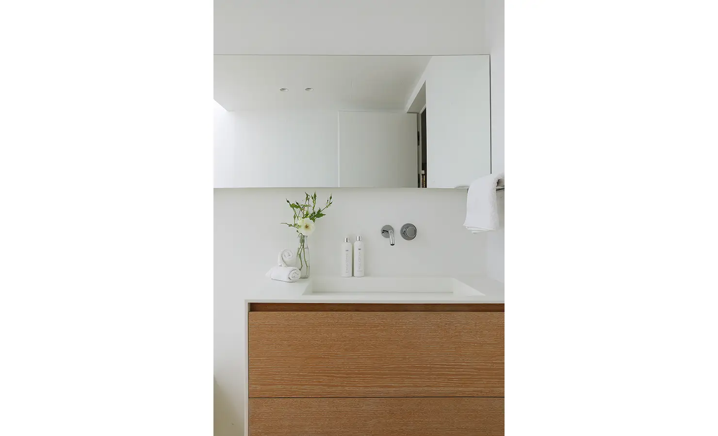 Perfect Hideaways A clean modern bathroom vanity with a wide mirror, simple white basin, light wood drawers, and a small vase of fresh flowers for a soft natural touch Pure Living, Bishopscourt
