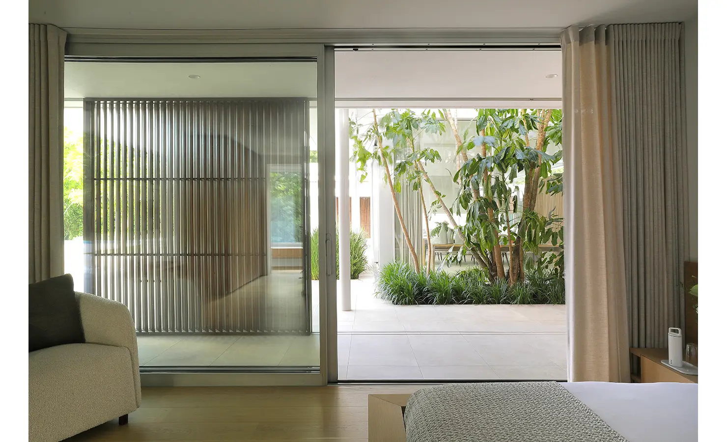 Perfect Hideaways A peaceful bedroom view through sliding glass doors to a lush courtyard garden with tall green plants, framed by vertical timber screens Pure Living, Bishopscourt