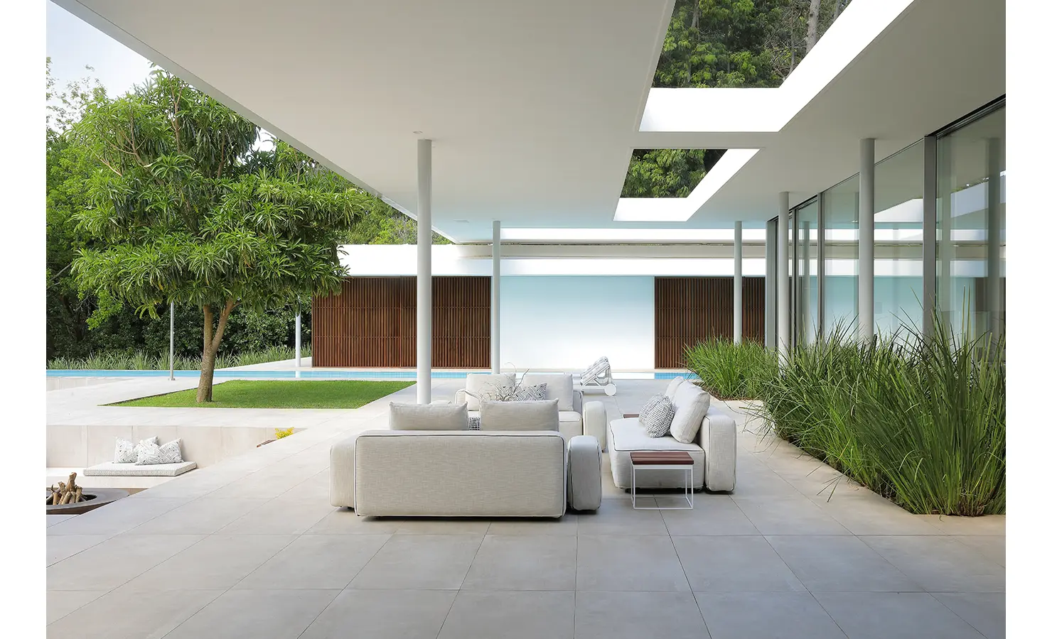 Perfect Hideaways A spacious outdoor terrace with soft white modular sofas, manicured planting, and a sculptural tree beneath a modern overhang with skylights Pure Living, Bishopscourt