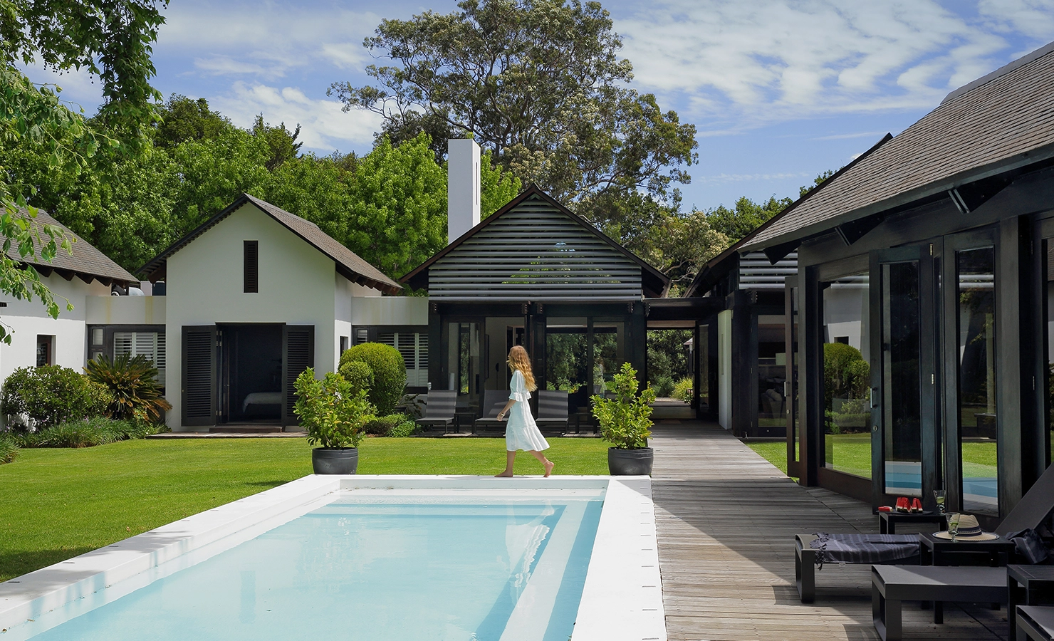 Perfect Hideaways contemporary Constantia villa with a swimming pool, timber deck, manicured garden, and modern gabled architecture, with a guest walking poolside on a sunny day, Tres Ossos, Constantia