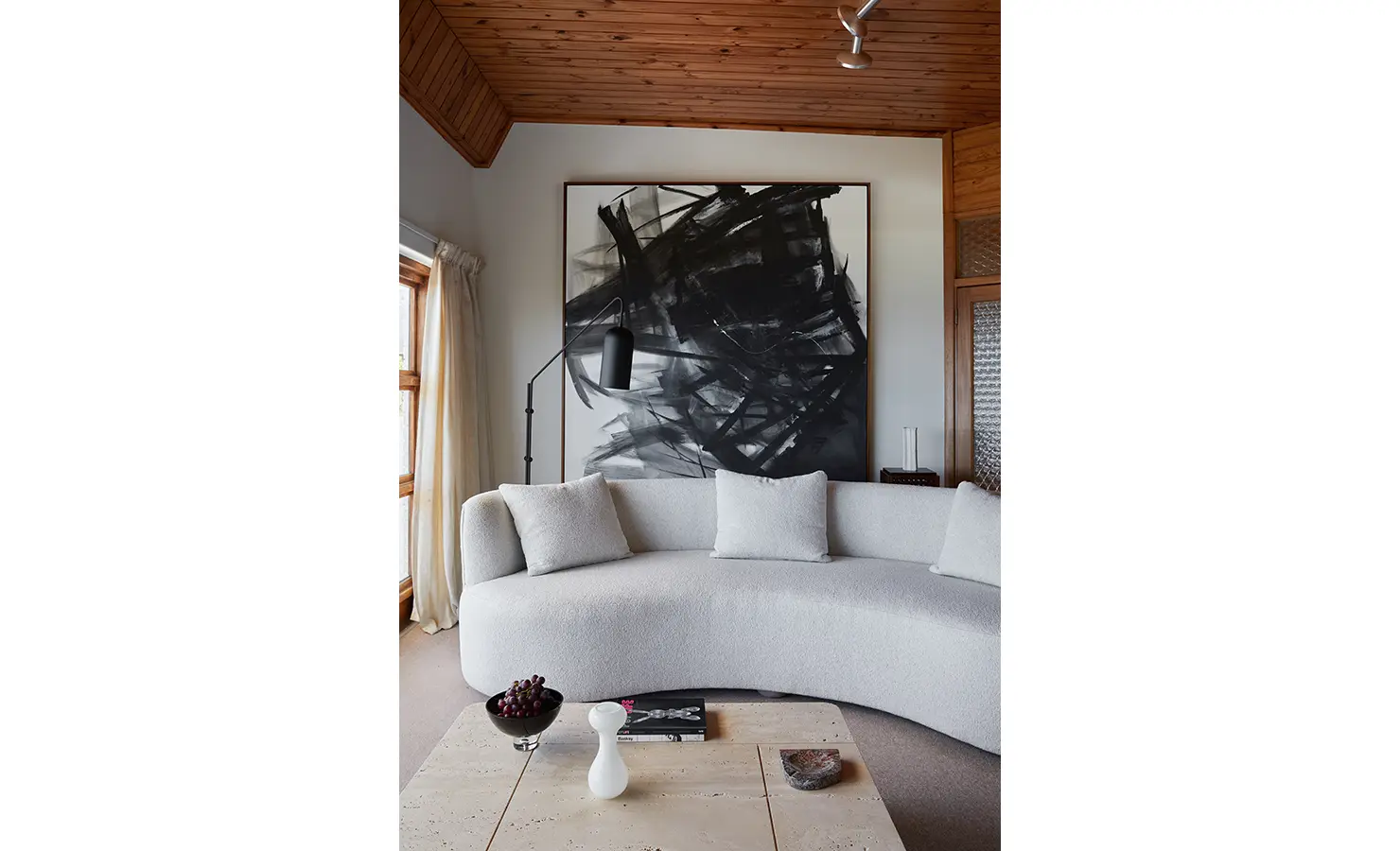 Perfect Hideaways a close view of the curved cream sofa set before a dramatic black abstract painting, soft natural light filtering through curtains, and a simple coffee table styled with books, fruit, and sculptural decor Camps Bay, The Liminal