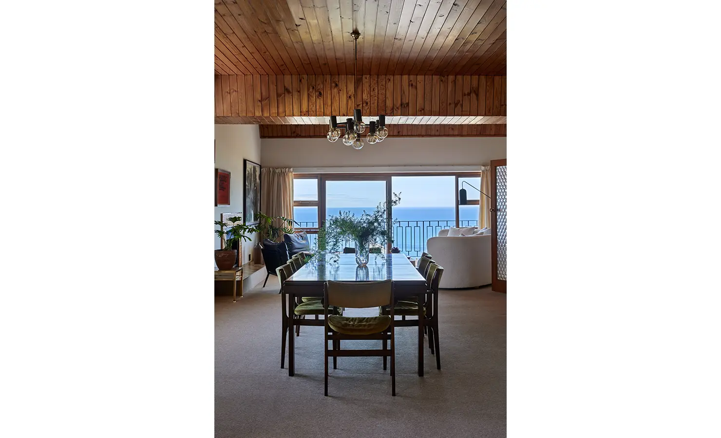 Perfect Hideaways a dining room with a long wooden table, mid-century chairs, fresh greenery as a centrepiece, and striking ocean views through large windows beneath a wooden ceiling Camps Bay, The Liminal