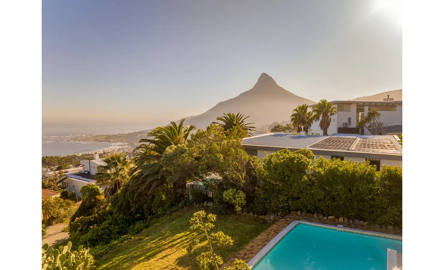 Perfect Hideaways a sweeping view of the coastline and mountains at golden hour, with lush greenery and a turquoise pool in the foreground and Lion’s Head rising in the distance Camps Bay, The Liminal