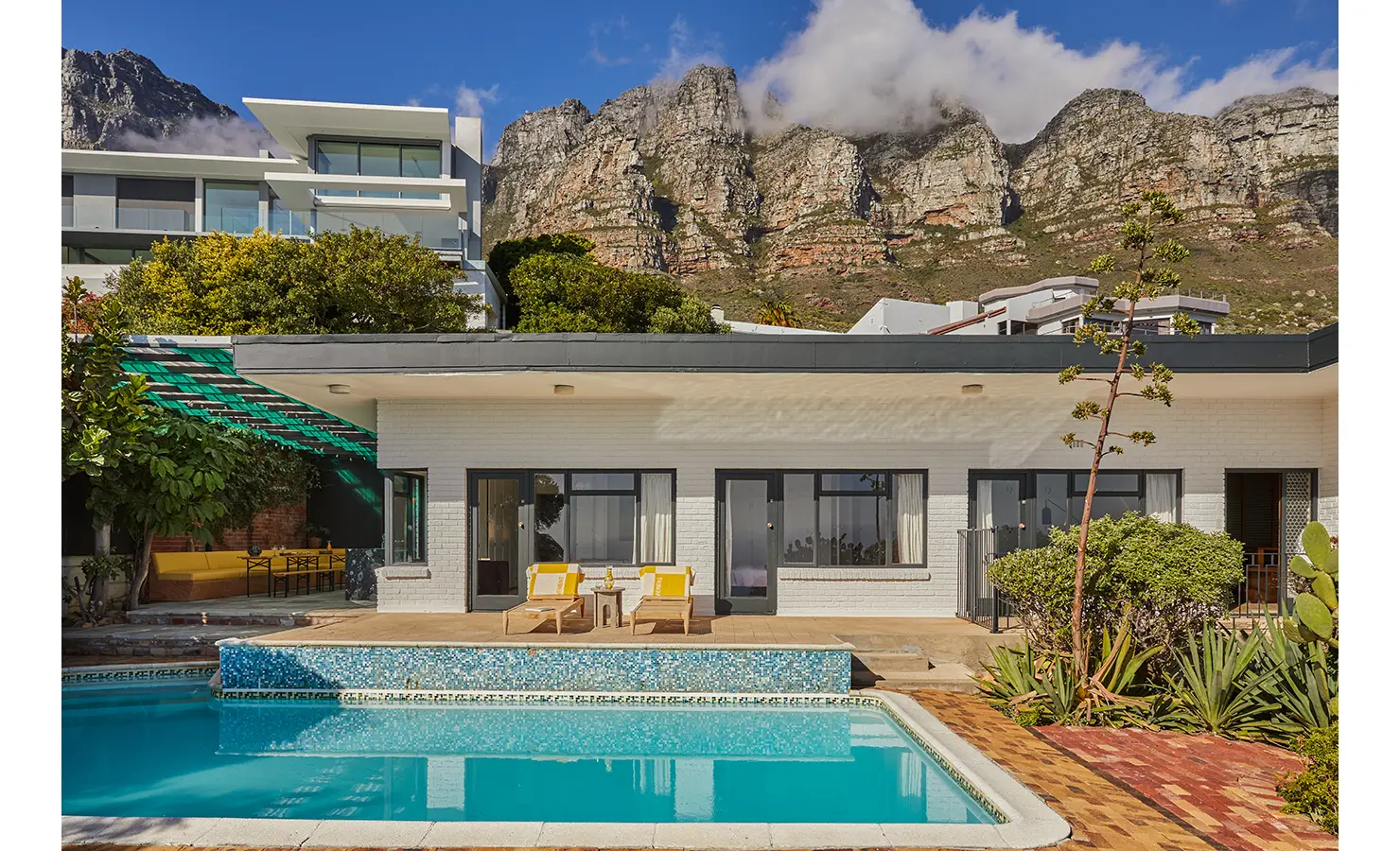 Perfect Hideaways an exterior view of the home with a sparkling pool in the foreground, modernist architecture, lush plants, and the dramatic rocky peaks of the Twelve Apostles rising overhead Camps Bay, The Liminal