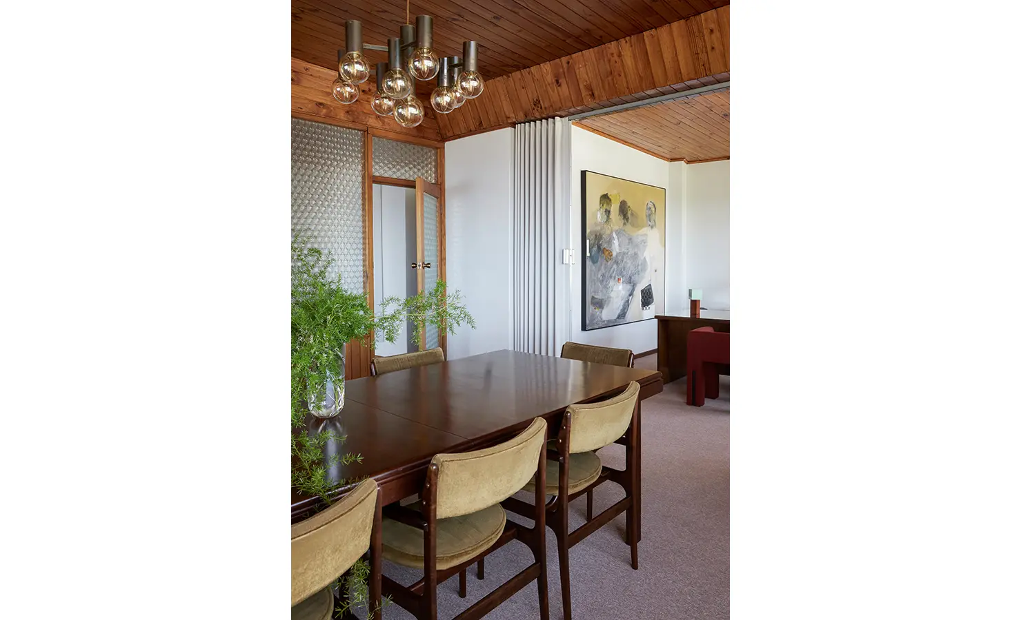 Perfect Hideaways a warm dining room with a polished wooden table, vintage upholstered chairs, lush greenery centerpiece, textured glass doors, and expressive contemporary artwork on the wall beneath a wooden ceiling Camps Bay, The Liminal