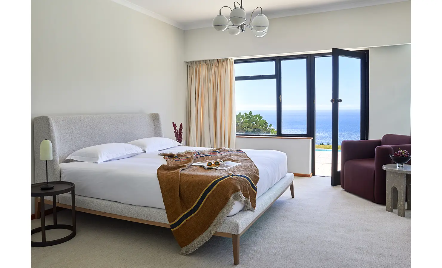 Perfect Hideaways a calm and airy bedroom with a soft upholstered bed, warm throw blanket, modern light fixture, and sweeping ocean views through large glass doors Camps Bay, The Liminal