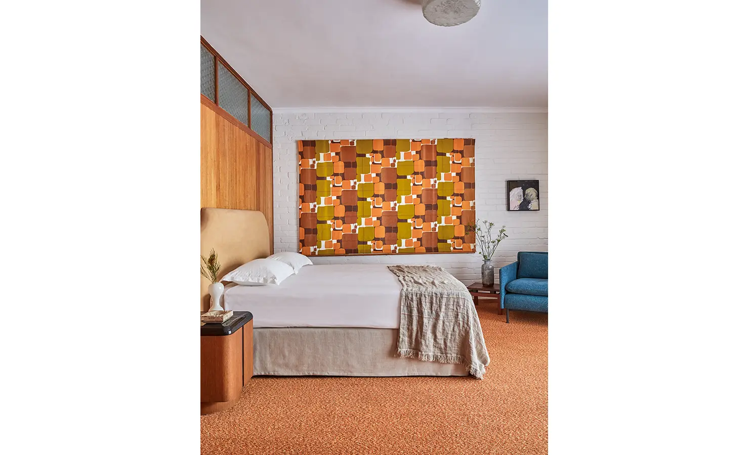 Perfect Hideaways a warm retro-inspired bedroom featuring a neutral bed, wood-panelled wall, textured orange carpet, and a bold geometric tapestry in earthy tones acting as a vibrant focal point above the bed Camps Bay, The Liminal