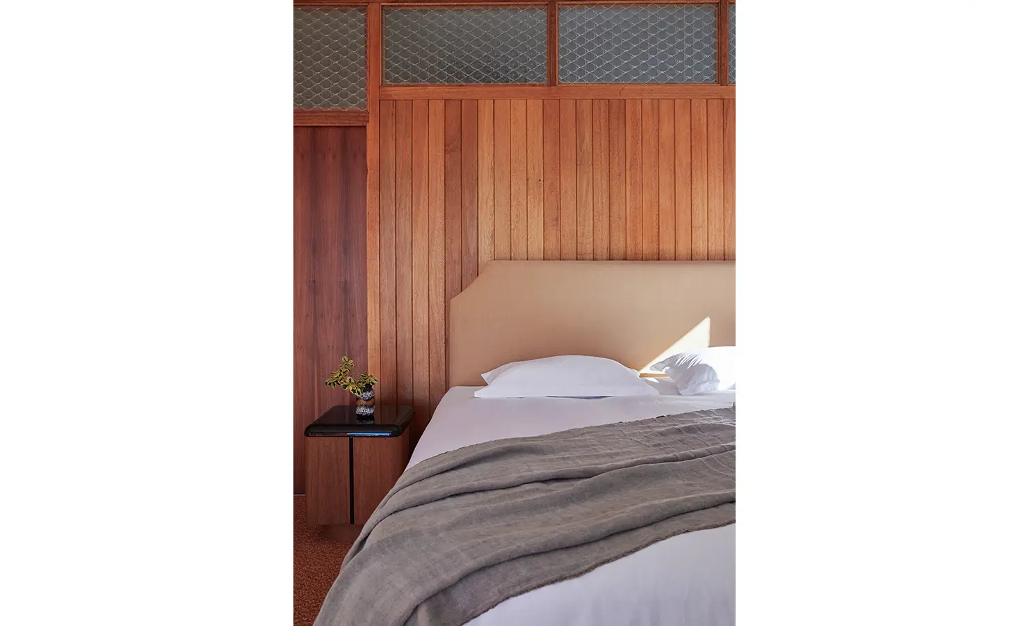 Perfect Hideaways a close view of the retro-paneled bedroom, highlighting the warm vertical wood planks, curved upholstered headboard, soft grey throw, and vintage glass-panel detailing above the wall Camps Bay, The Liminal