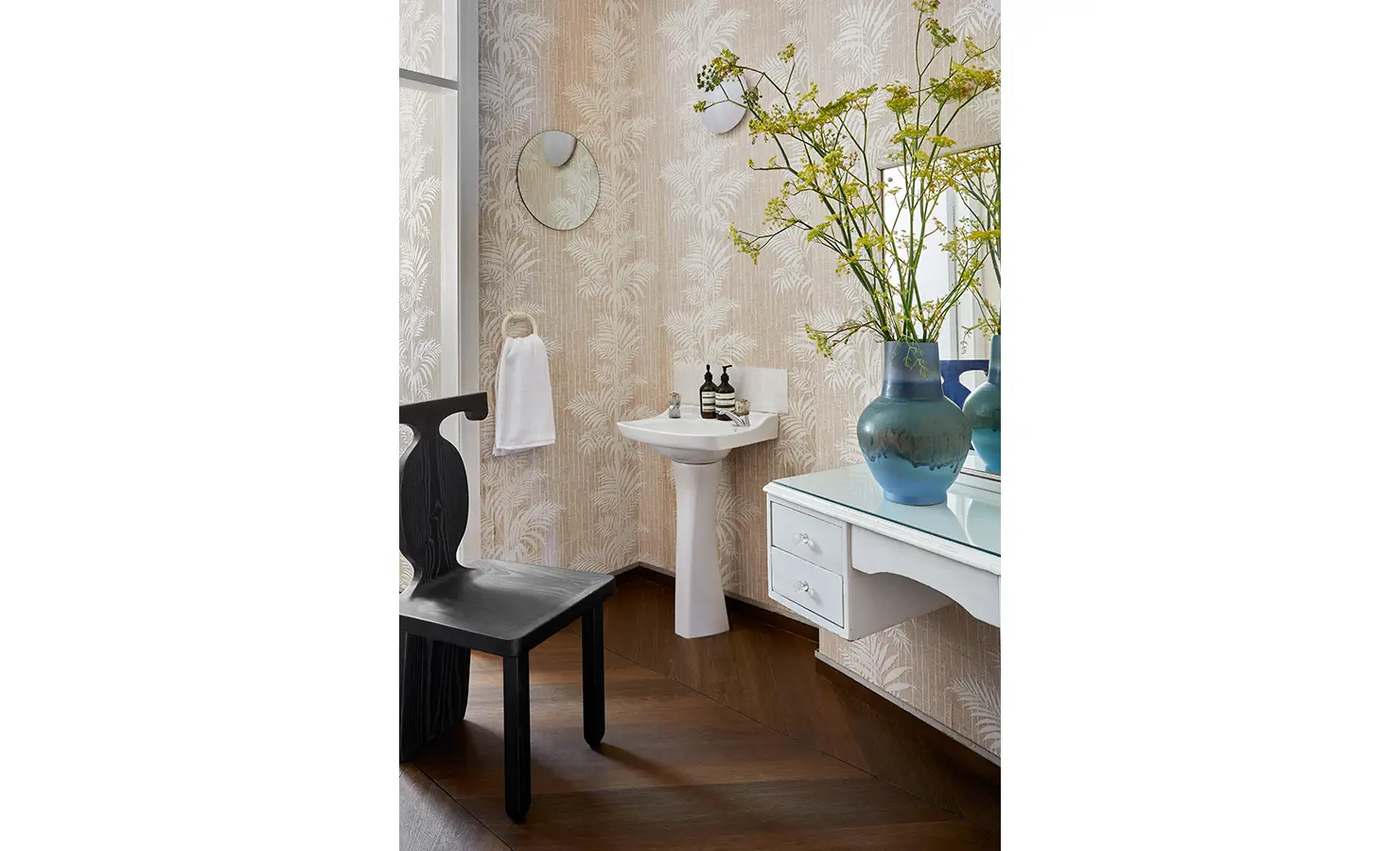 Perfect Hideaways a soft vintage-inspired bathroom with palm-patterned wallpaper, pedestal sink, round mirror, bright blue ceramic vase with wild botanical stems, and a black sculptural chair Camps Bay, The Liminal