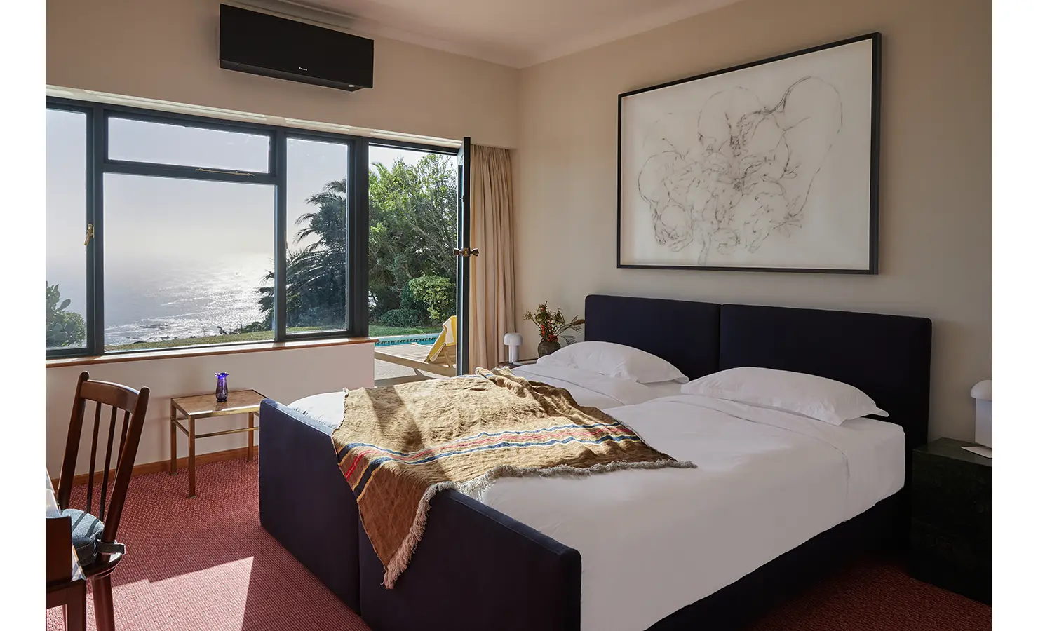 Perfect Hideaways a calm bedroom with twin beds in a deep navy frame, airy curtains, warm throw blanket, and wide coastal views through expansive windows Camps Bay, The Liminal