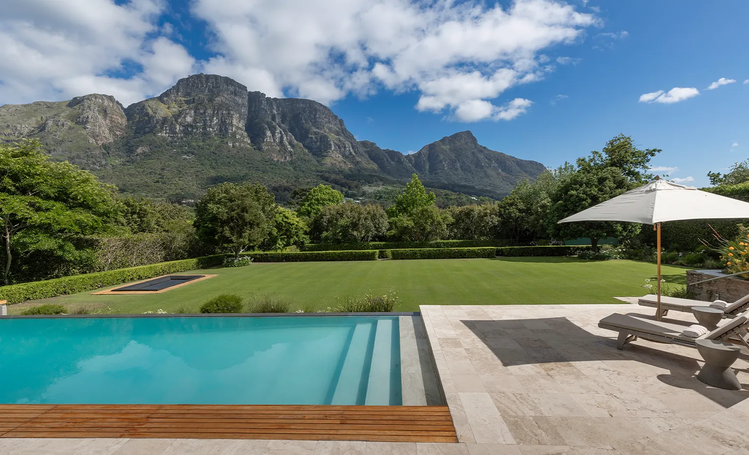 Perfect Hideaways luxury outdoor pool terrace overlooking manicured lawn and dramatic mountain views with sun loungers and umbrella at a tranquil garden setting, Bishopscourt, Botanical Villa
