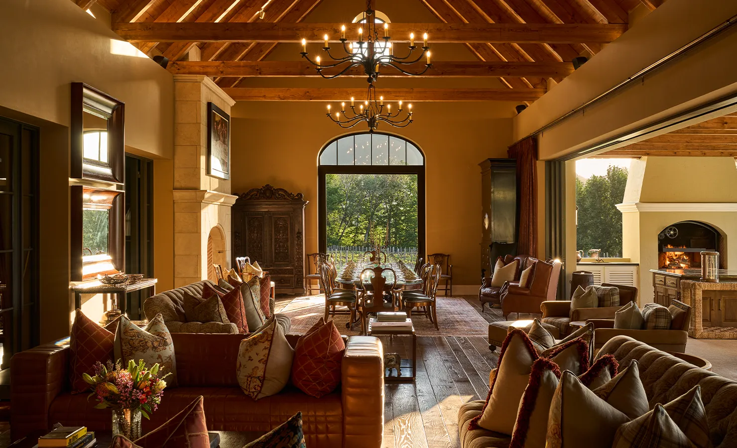 Perfect Hideaways luxurious open-plan living and dining area with vaulted wooden ceilings, chandeliers, leather sofas, fireplace and large arched windows overlooking lush gardens Paddakloof, Franschhoek