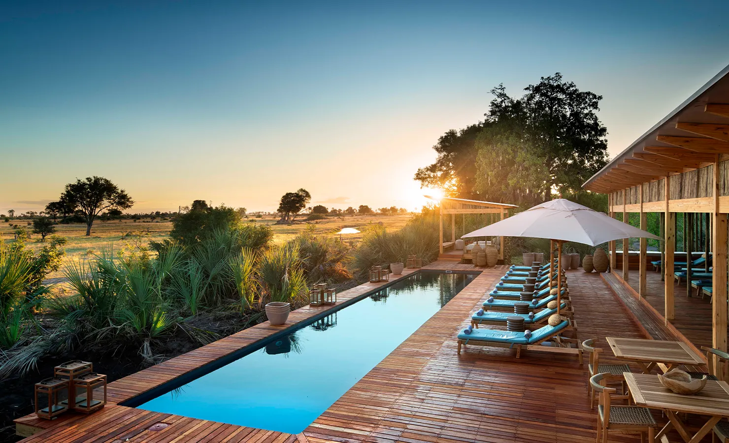 Perfect Hideaways luxury safari lodge with wooden deck and infinity pool overlooking the Okavango Delta at sunset with sun loungers and open savannah views, Tawana, Moremi Game reserve