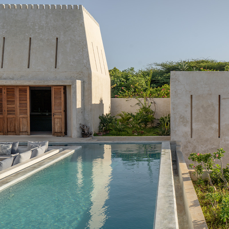 Perfect Hideaways serene courtyard swimming pool with sunken lounge seating, natural stone walls, wooden shutters and lush tropical garden surrounds at House E, Lamu