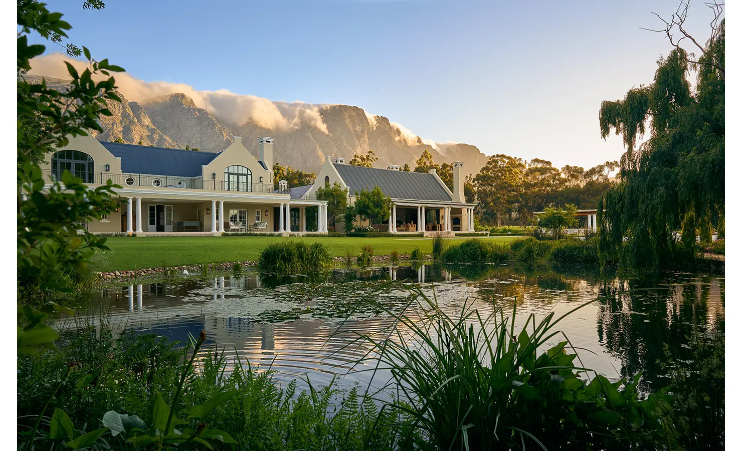 Perfect Hideaways grand Cape Winelands estate with manicured lawns, tranquil pond and dramatic mountain backdrop at sunset Paddakloof, Franschhoek
