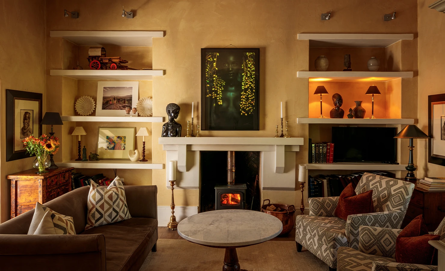 Perfect Hideaways elegant lounge with wood-burning fireplace, warm lighting, built-in shelves with art and décor, comfortable armchairs and sofa creating a cosy sitting area, The Manor, Franschhoek