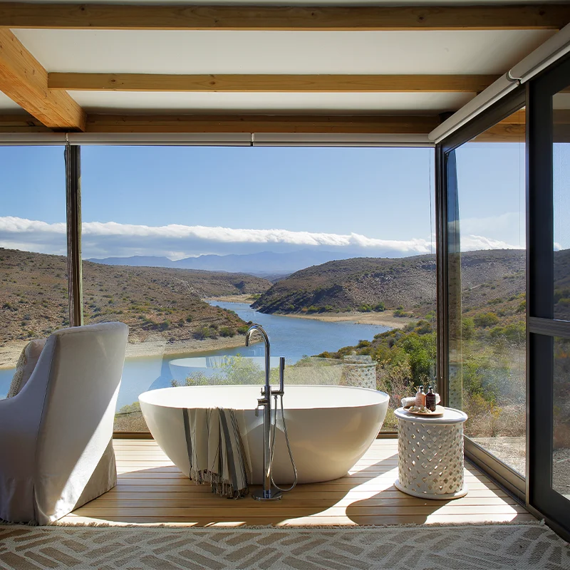 Perfect Hideaways freestanding bathtub and lounge chair set before floor-to-ceiling glass overlooking the winding Brandrivier and rugged Karoo landscape Berghuisie, Brandrivier
