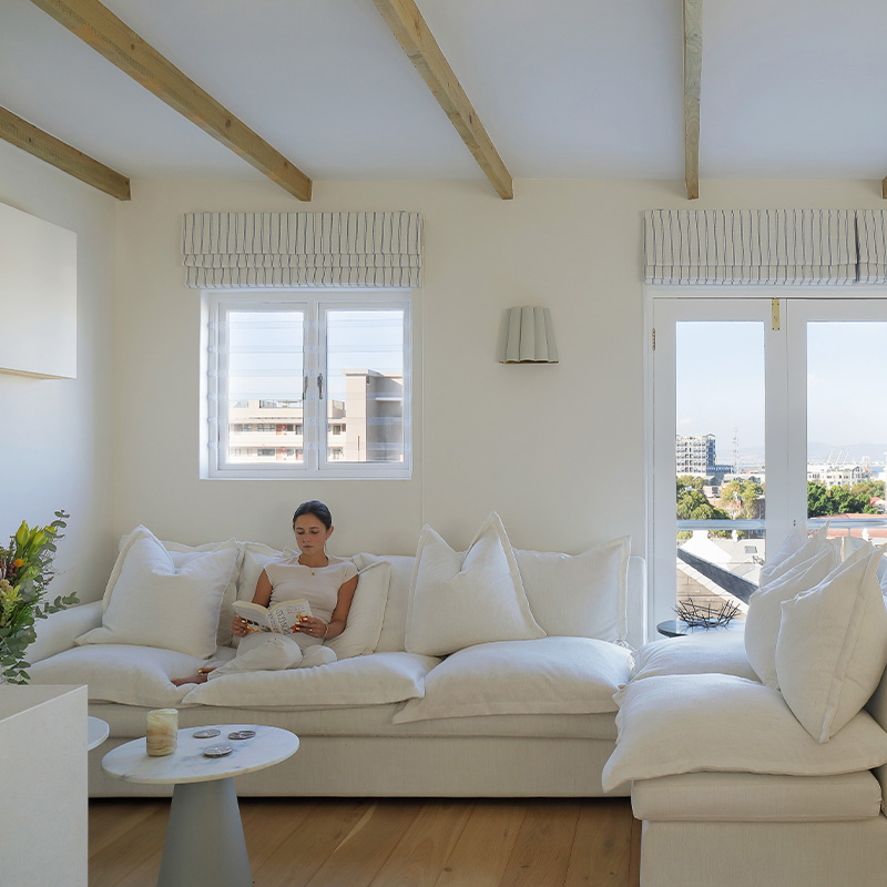 Perfect Hideaways light-filled living room with a woman reading on a plush white sofa, large windows and French doors opening to city views, Silhouette, De Waterkant