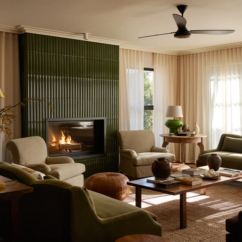 Perfect Hideaways a warm, elegant living room featuring a modern fireplace set into a tall green tiled wall, surrounded by soft neutral armchairs, olive-toned sofas, natural wood tables, layered ceramics, and sunlight filtering through sheer cream curtains, creating a serene and sophisticated space Colmant Manor House, Franschoek