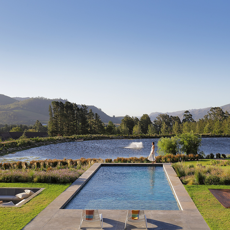 Perfect Hideaways grand luxury lakehouse with illuminated terraces, expansive balconies and mountain backdrop overlooking a landscaped garden and pool at dusk, The Lakehouse on Val Du Lac, Franschhoek