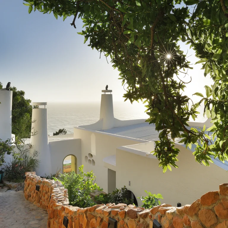 Perfect Hideaways coastal villa framed by lush trees and stone pathways overlooking the ocean in warm golden sunlight, Perfect Hideaways Blog
