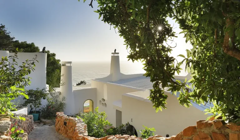 Perfect Hideaways coastal villa framed by lush trees and stone pathways overlooking the ocean in warm golden sunlight, Perfect Hideaways Blog