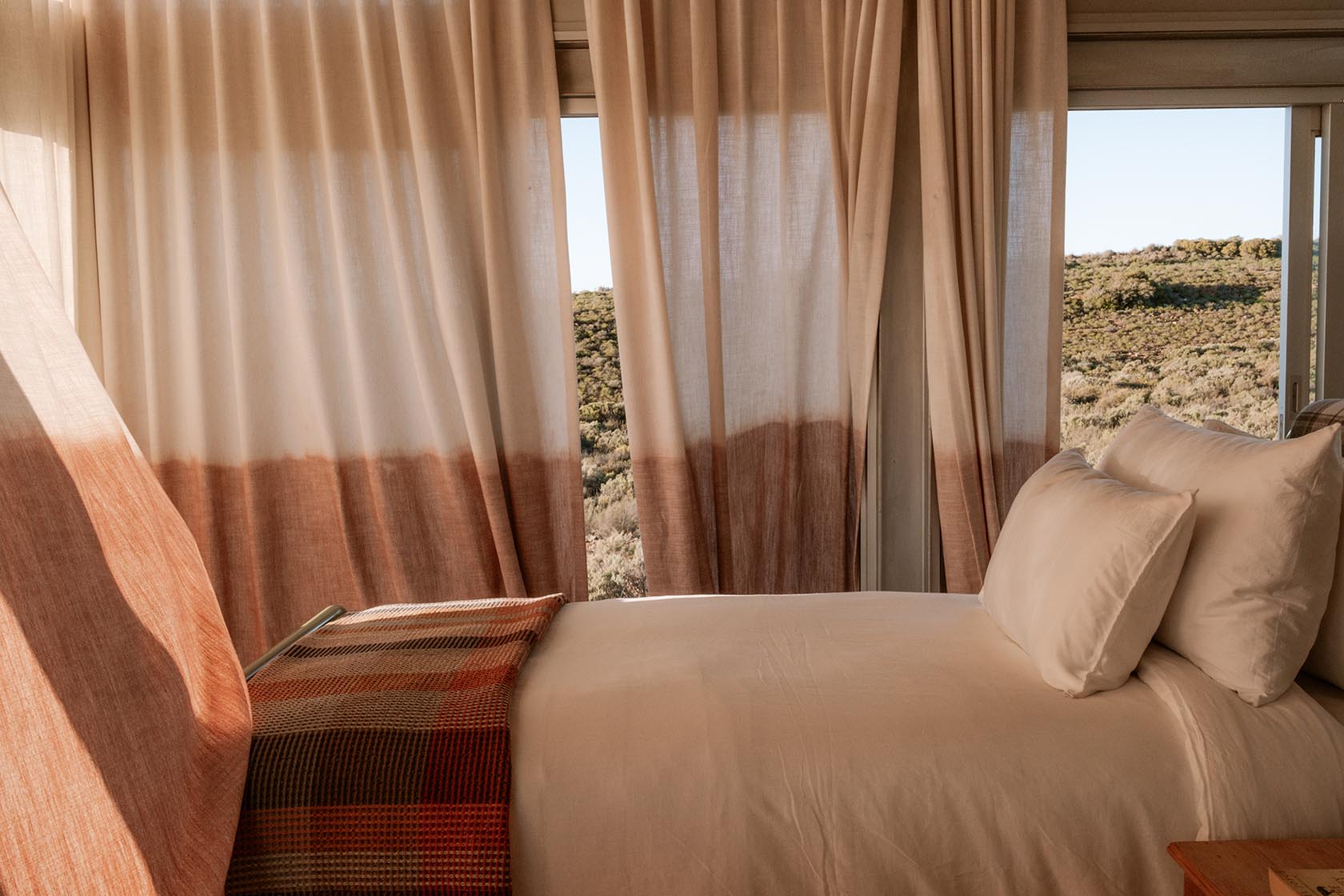 Perfect Hideaways cosy bedroom with soft linen curtains, warm tones and expansive Karoo views, Jackals Rest, Montagu.